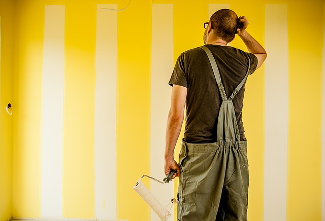 mężczyzna stojący z wałkiem do malowania przed żółtą ścianą